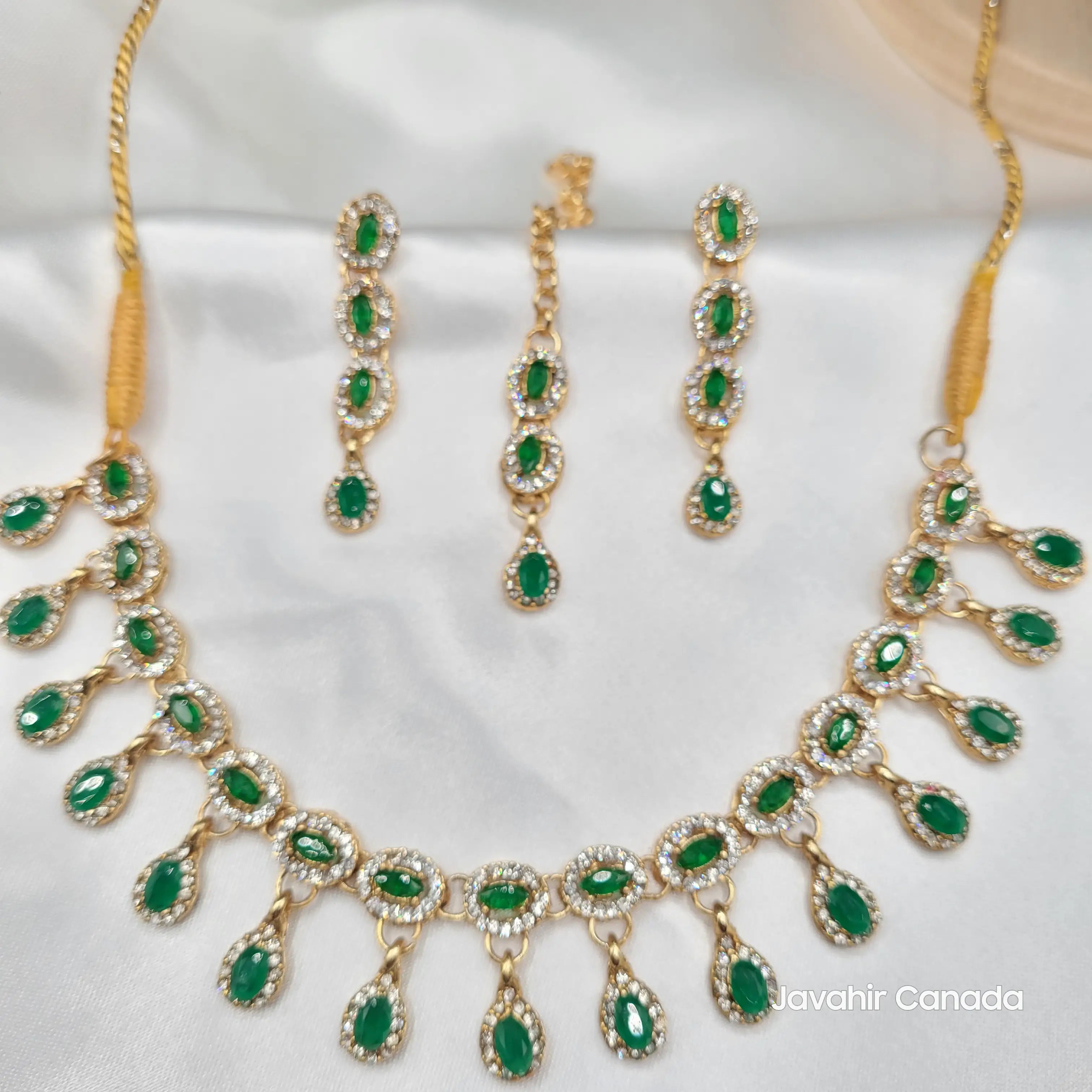 Full Daint necklace set with emerald green stones and long drop earrings on white satin