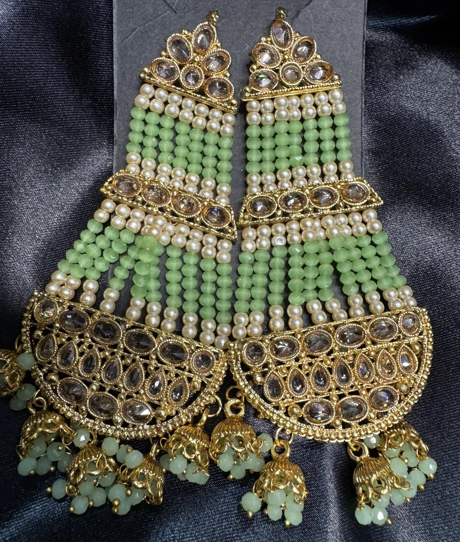Ornate green and gold earrings with pearl-like beads on a dark fabric background