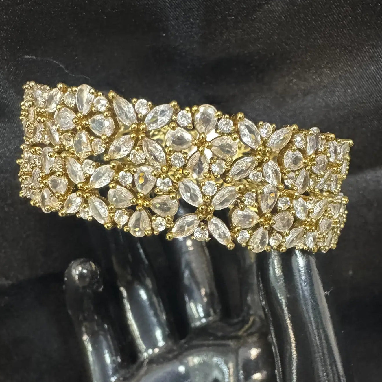 Gold-plated bangles with clear gemstones and flower patterns on a black hand sculpture