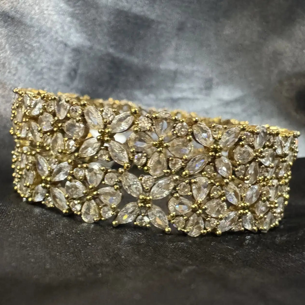 Gold-plated bangles with clear gemstones and flower patterns on a dark fabric background