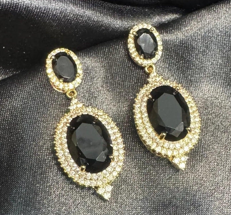 Pair of gold and black earrings on black satin fabric
