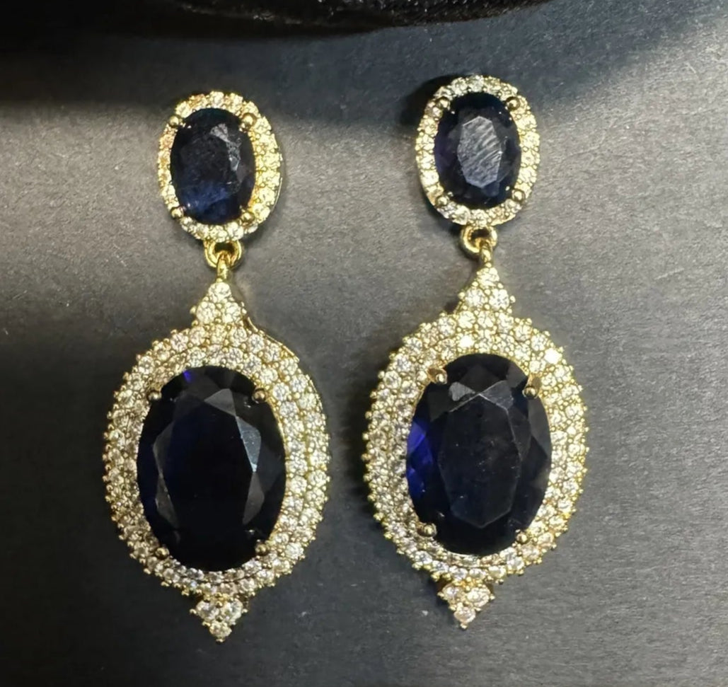 Pair of gold plated earrings with navy blue gemstones on a black satin background