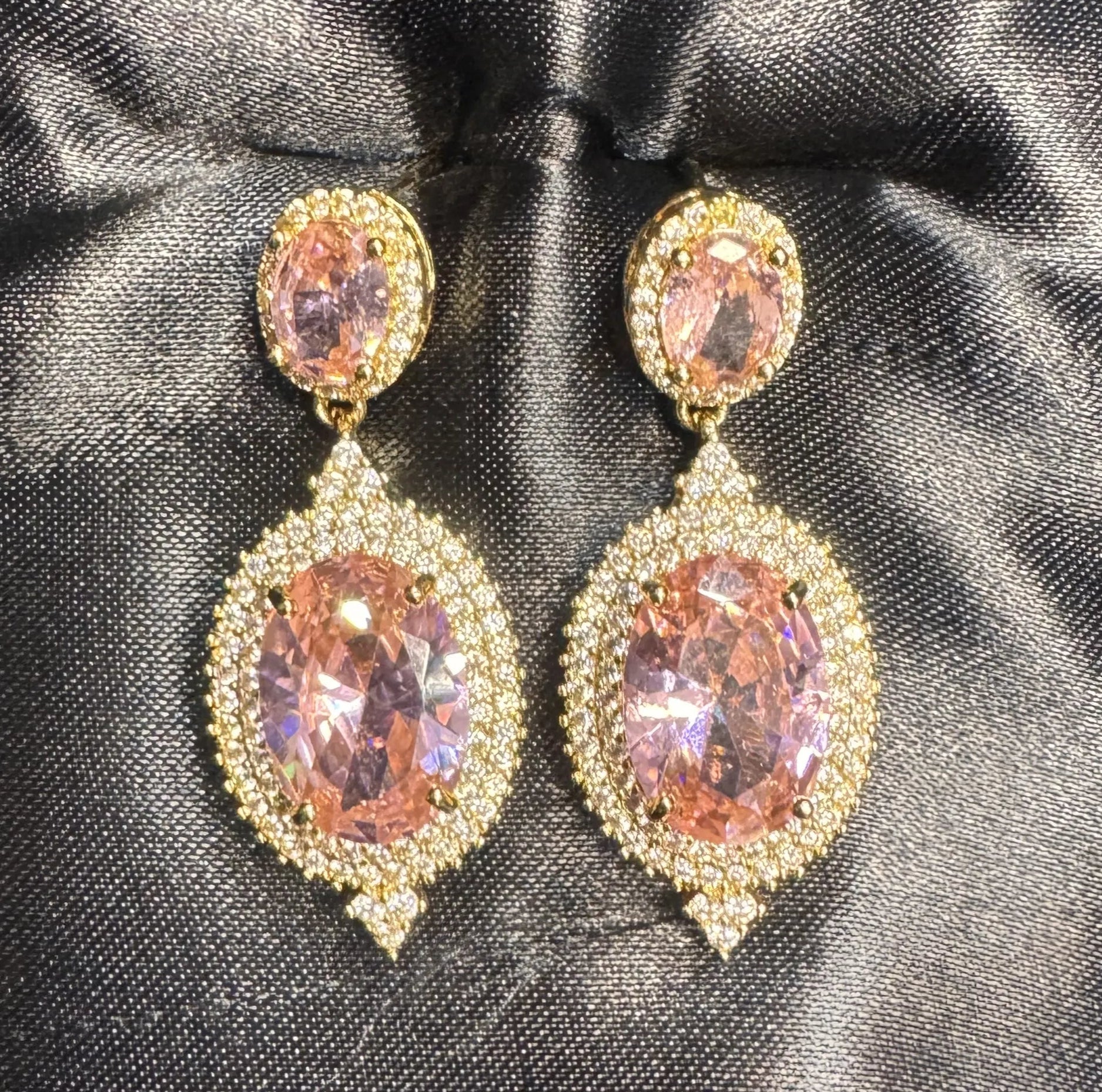 Ornate earrings with pink gemstones on a black satin background