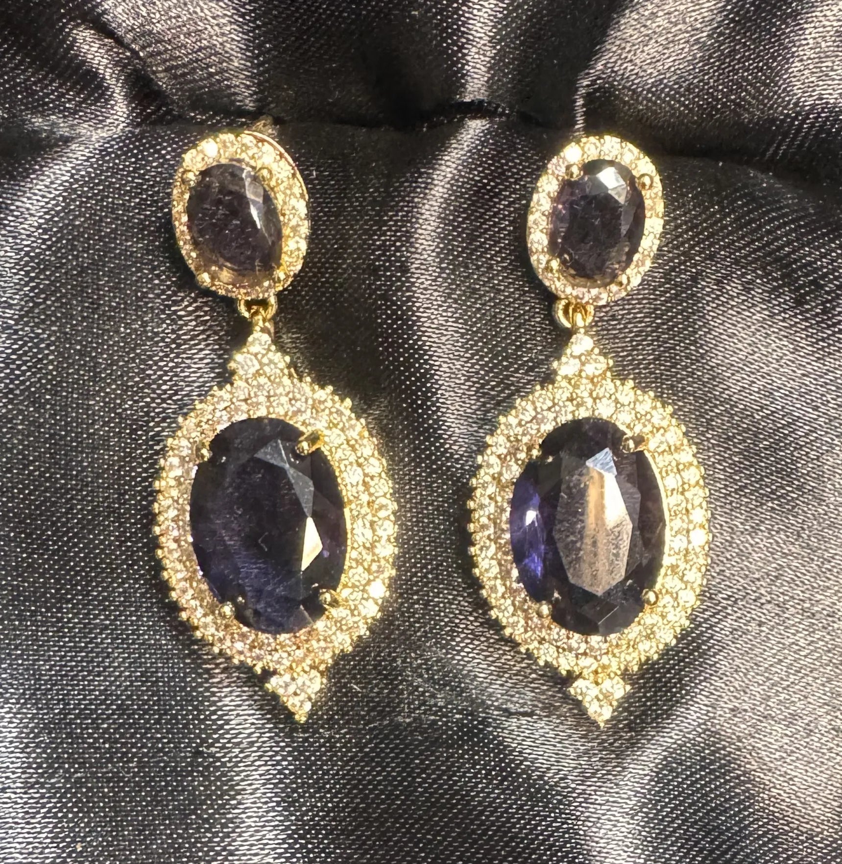 Pair of gold earrings with purple gemstones on a black satin background