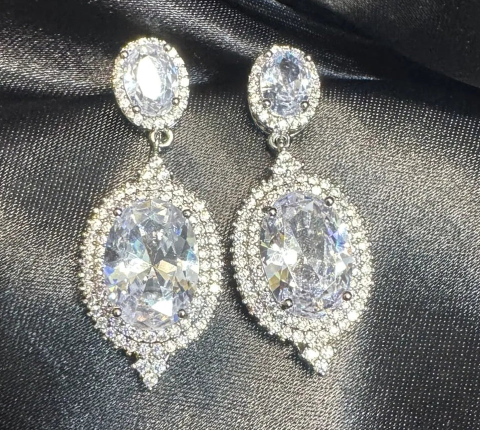 Silver earrings with clear gemstones on a black satin background