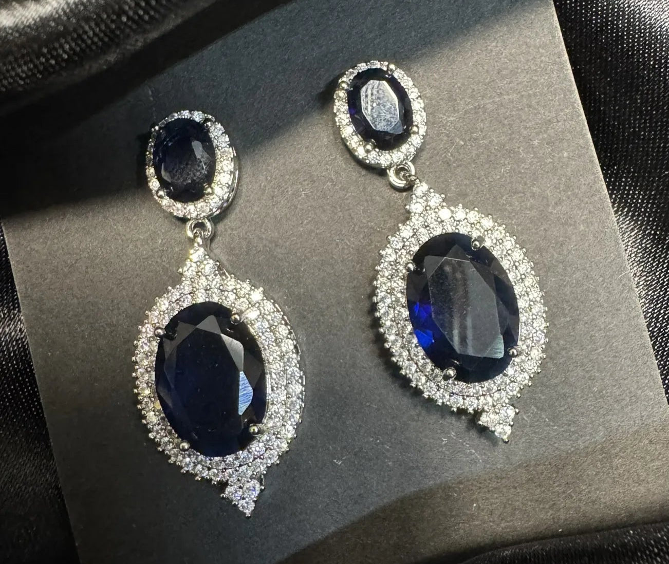 Pair of earrings with blue gemstones and silver accents on a dark fabric background