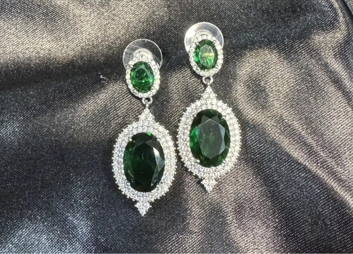 Pair of emerald green earrings on a dark fabric background
