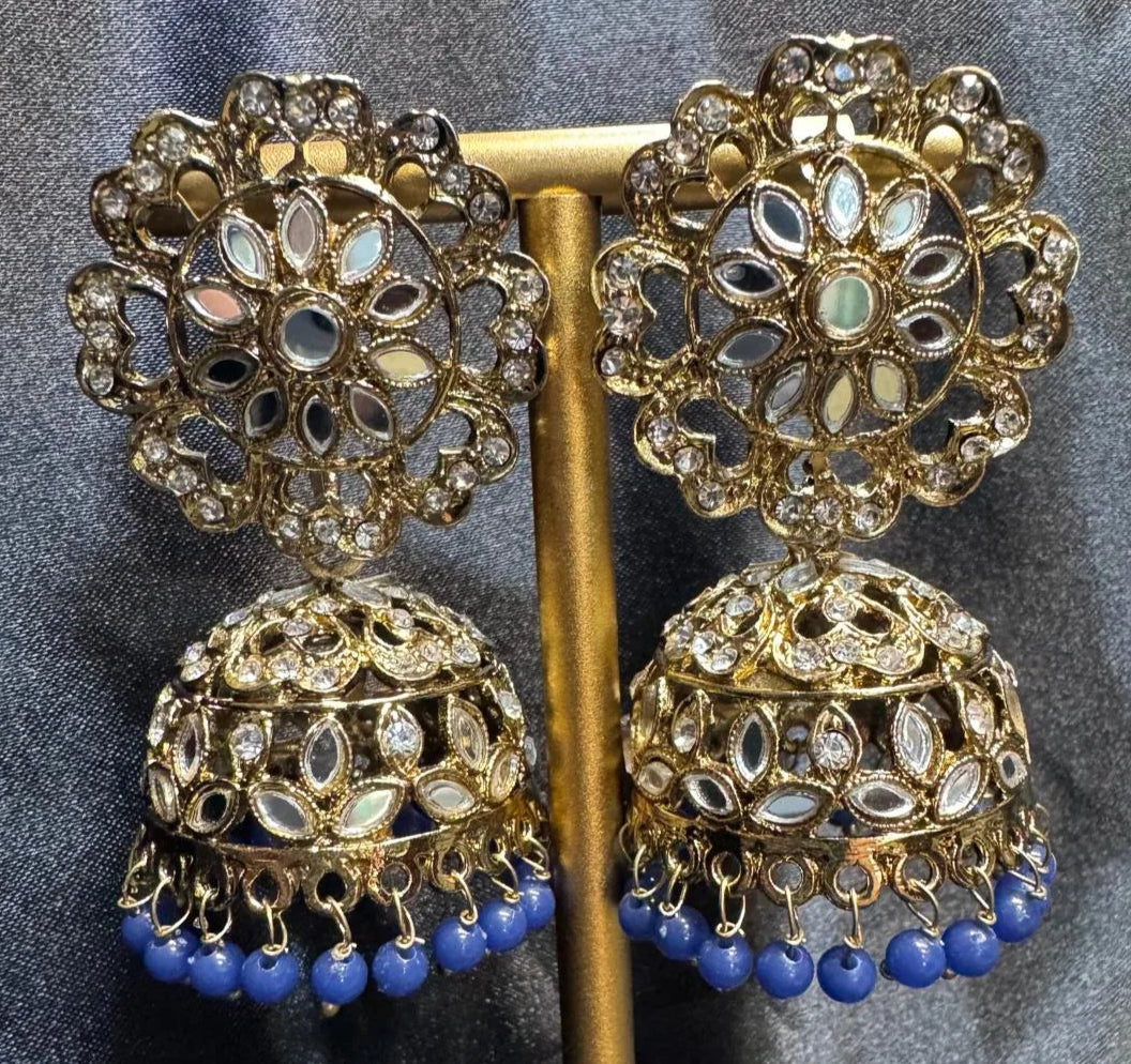 Ornate gold plated earrings/jhumka with blue beads on a dark fabric background