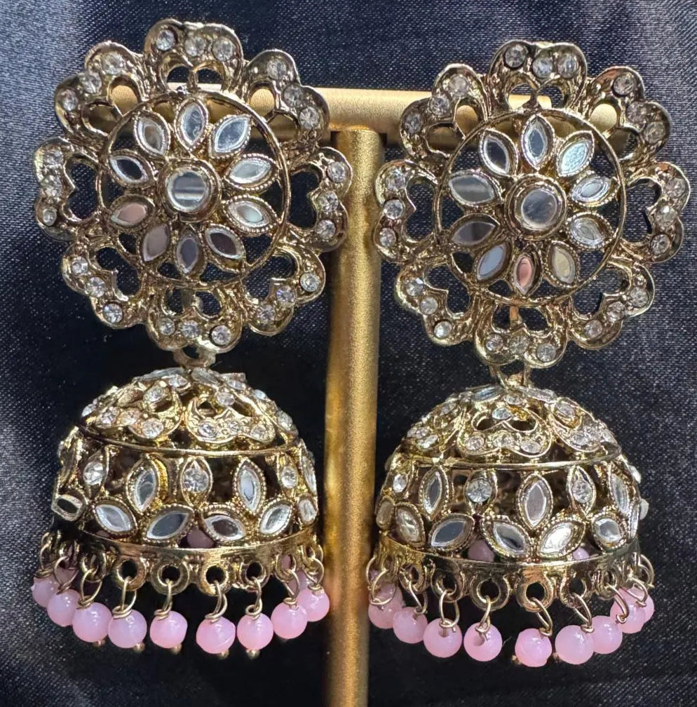 Ornate gold plated earrings/jhumka with light pink beads on a dark fabric background