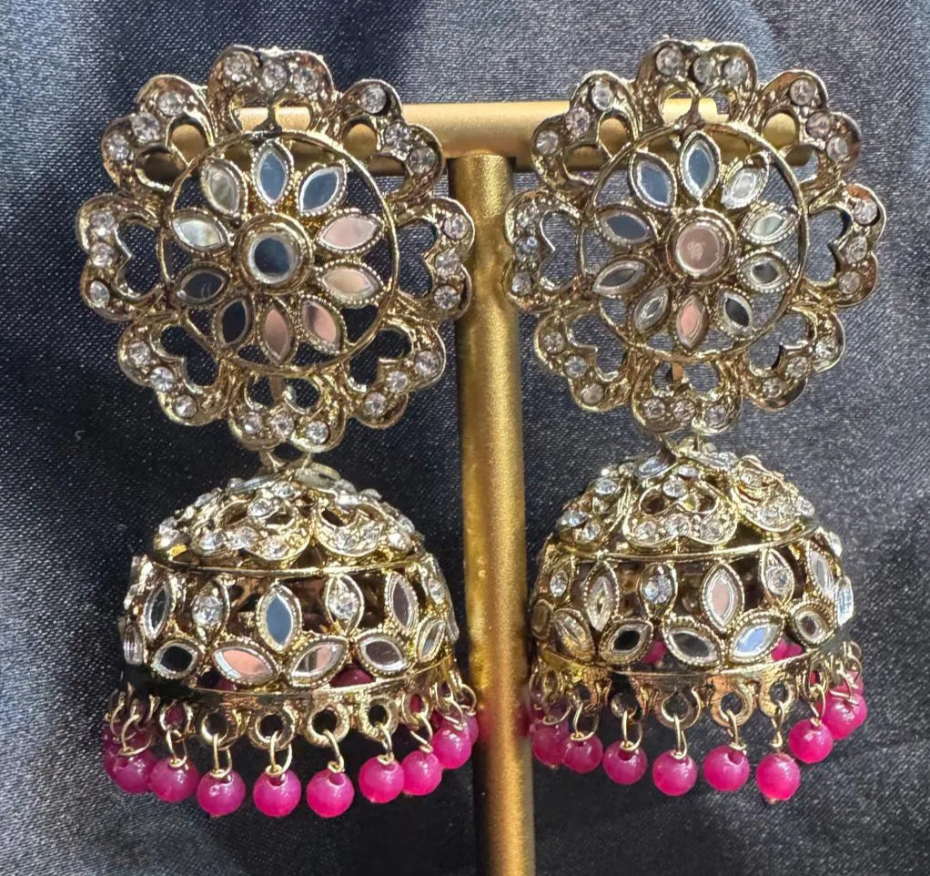 Ornate gold plated earrings/jhumka with magenta beads on a dark fabric background
