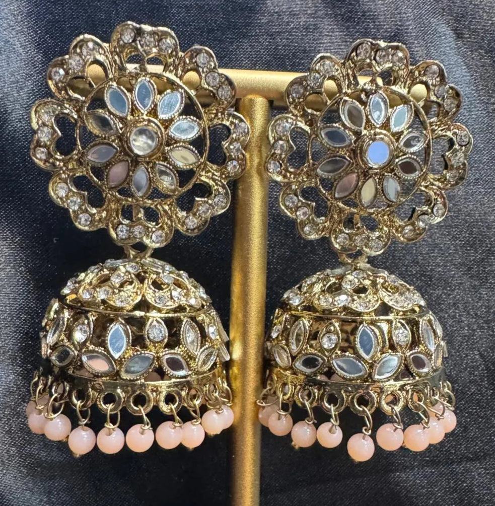 Ornate gold plated earrings/jhumka with peach beads on a dark fabric background