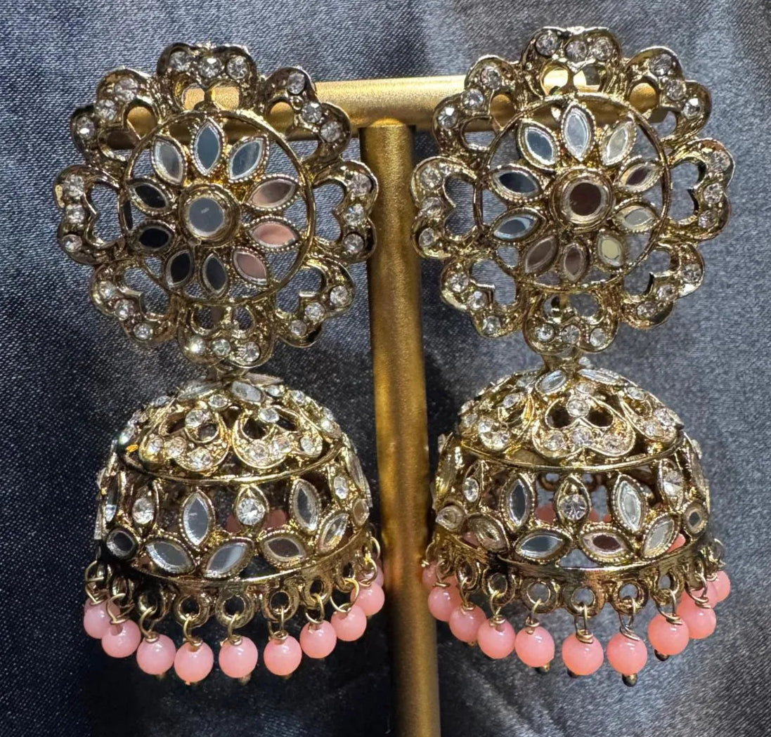 Ornate gold plated earrings with pink beads on a dark fabric background