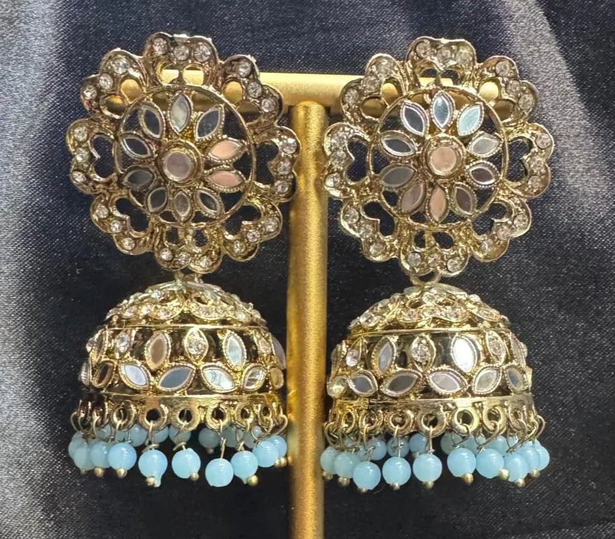 Ornate gold plated earrings/jhumka with teal beads on a dark fabric background