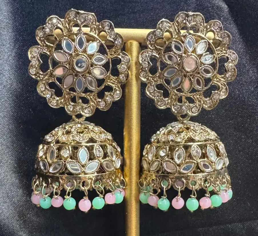 Ornate gold plated earrings/jhumka with teal and pink beads on a dark fabric background