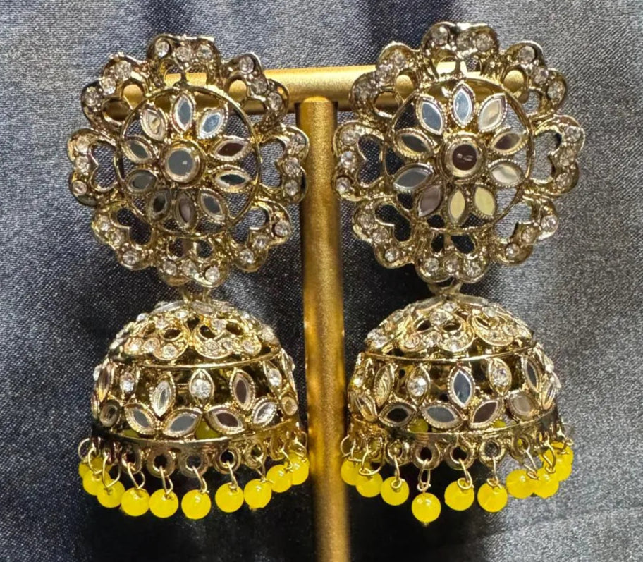 Ornate gold plated earrings/jhumka with yellow beads on a dark fabric background