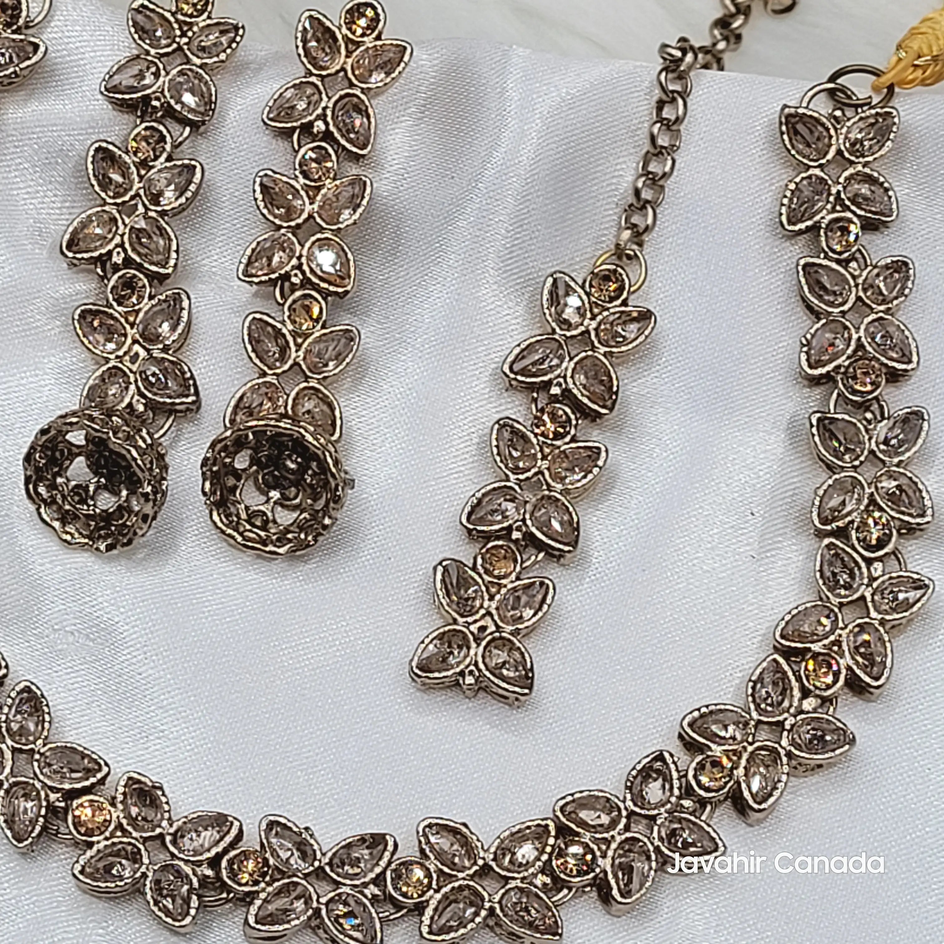 Close-up of champagne CZ floral necklace and earrings from the Flora set with teardrop and round marquise stones on white satin.