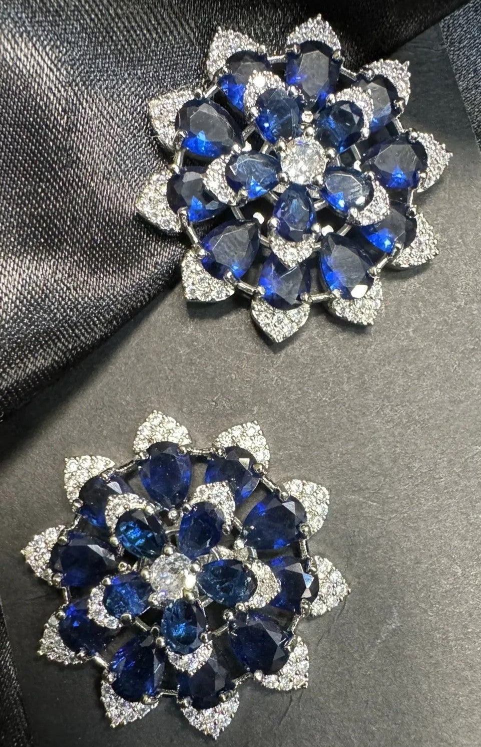 Pair of silver earrings with blue gemstones on a black satin background