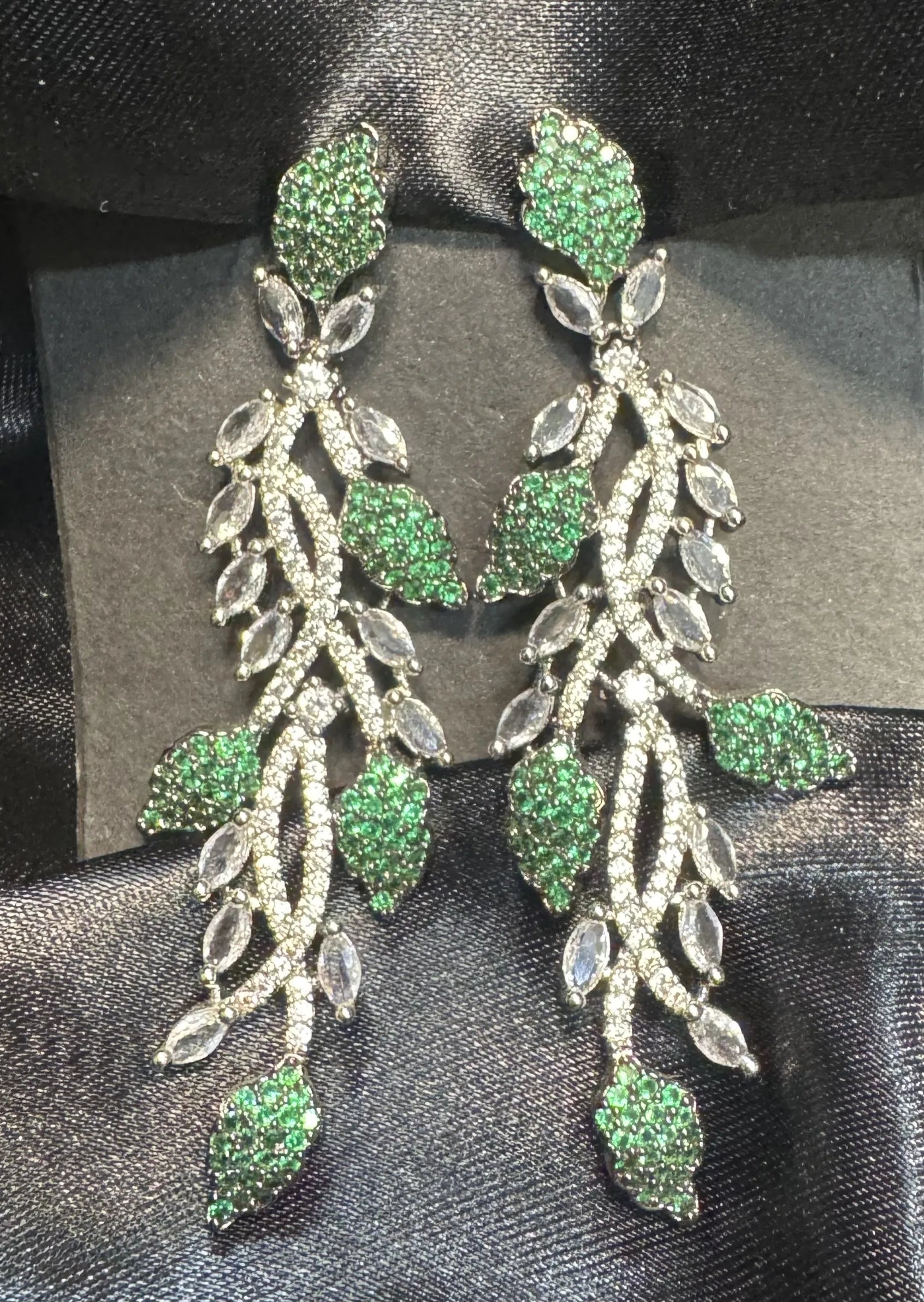 Green and silver leaf-shaped earrings on a black satin background