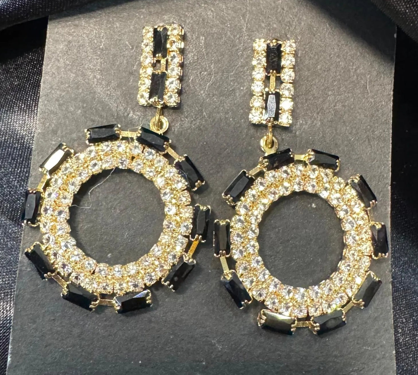 Pair of gold and black hoop American diamonds earrings on a gray card.