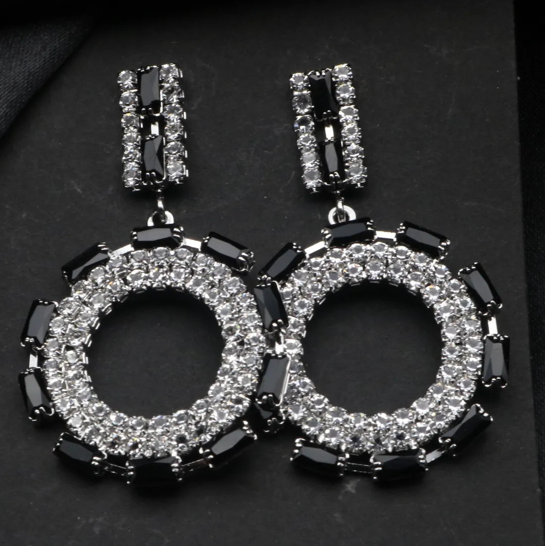 Pair of hoop American diamonds earrings with black and clear gemstones on a dark background