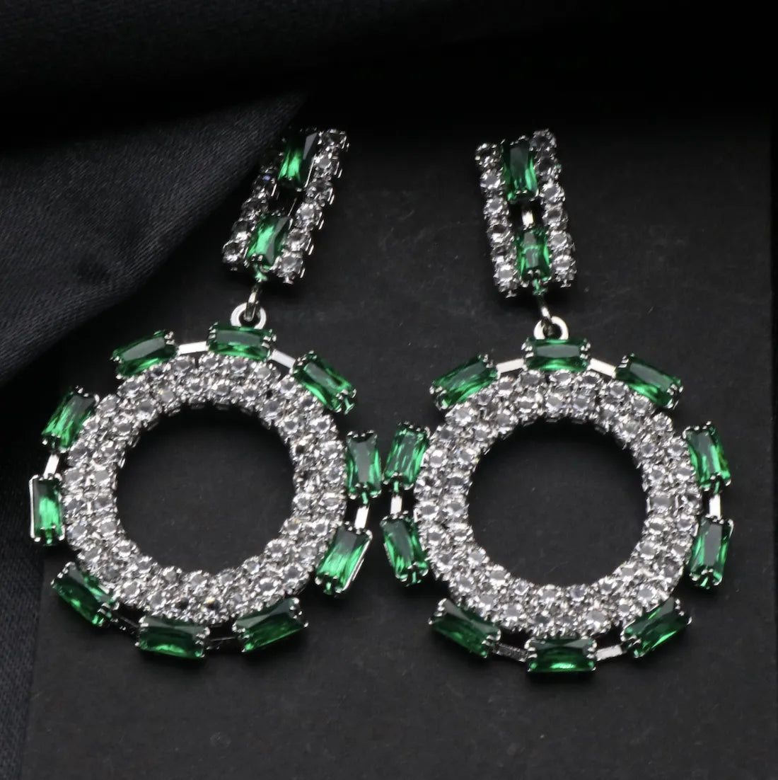 Green and silver hoop American diamonds earrings on a dark fabric background