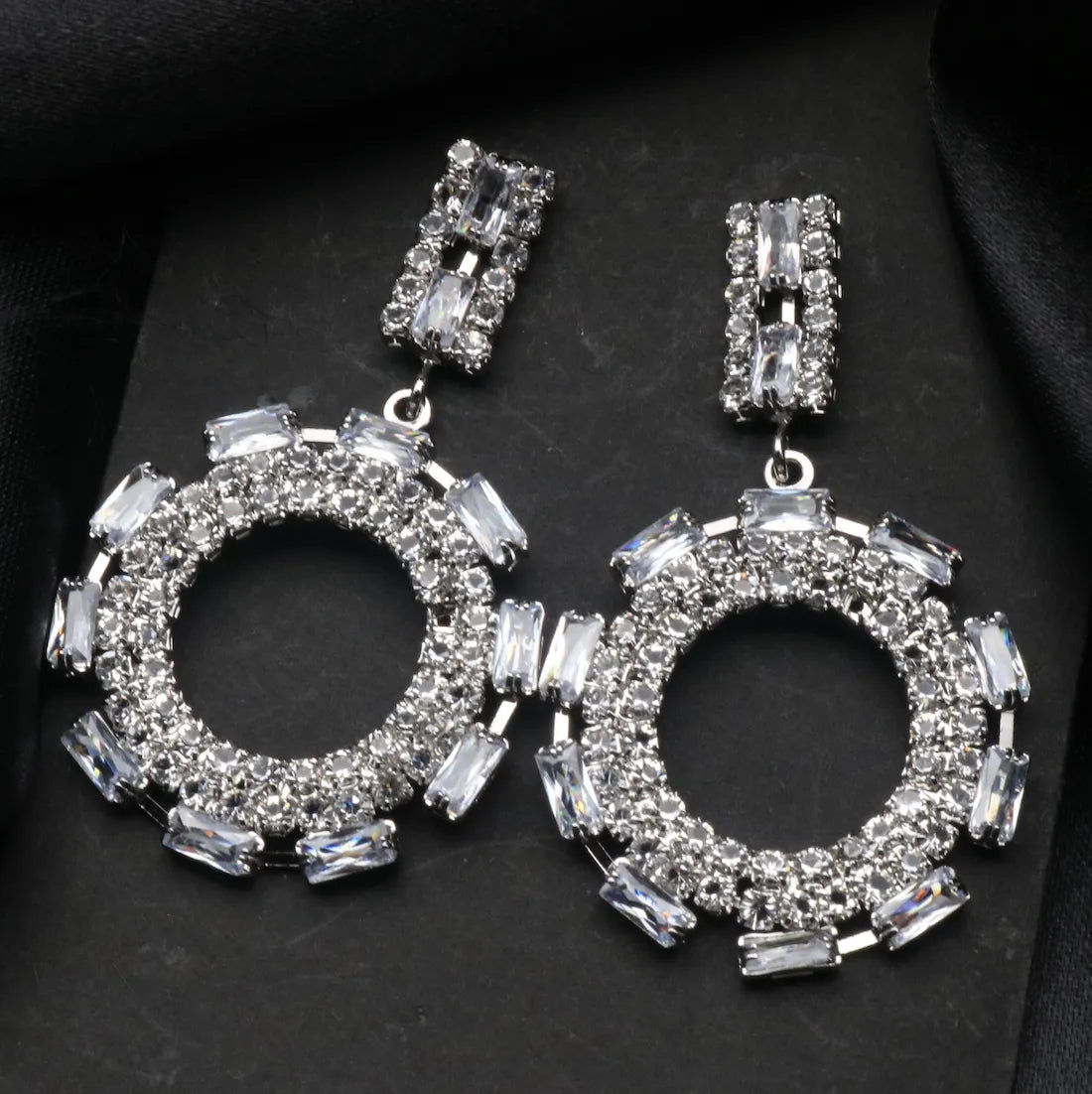 Silver hoop American diamonds earrings with clear gemstones on a black background