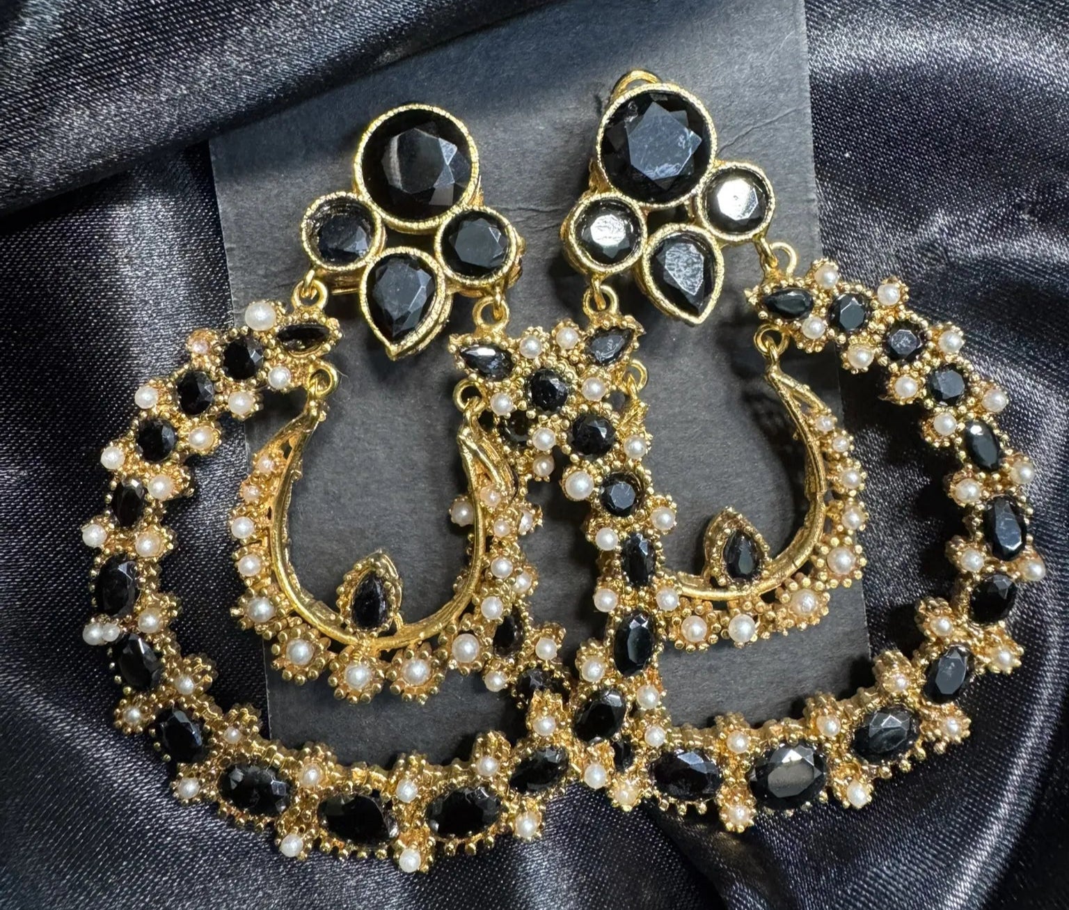 Ornate gold and black earrings on a dark fabric background