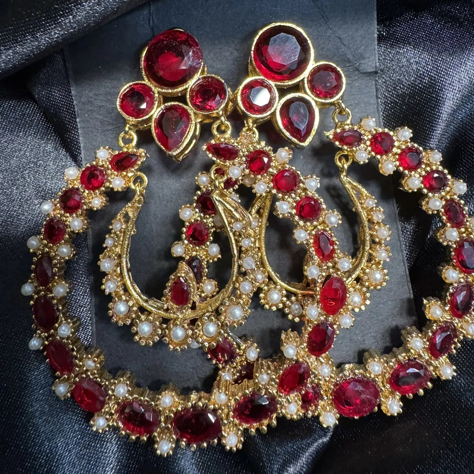 Ornate gold earrings with red gemstones on a black satin background