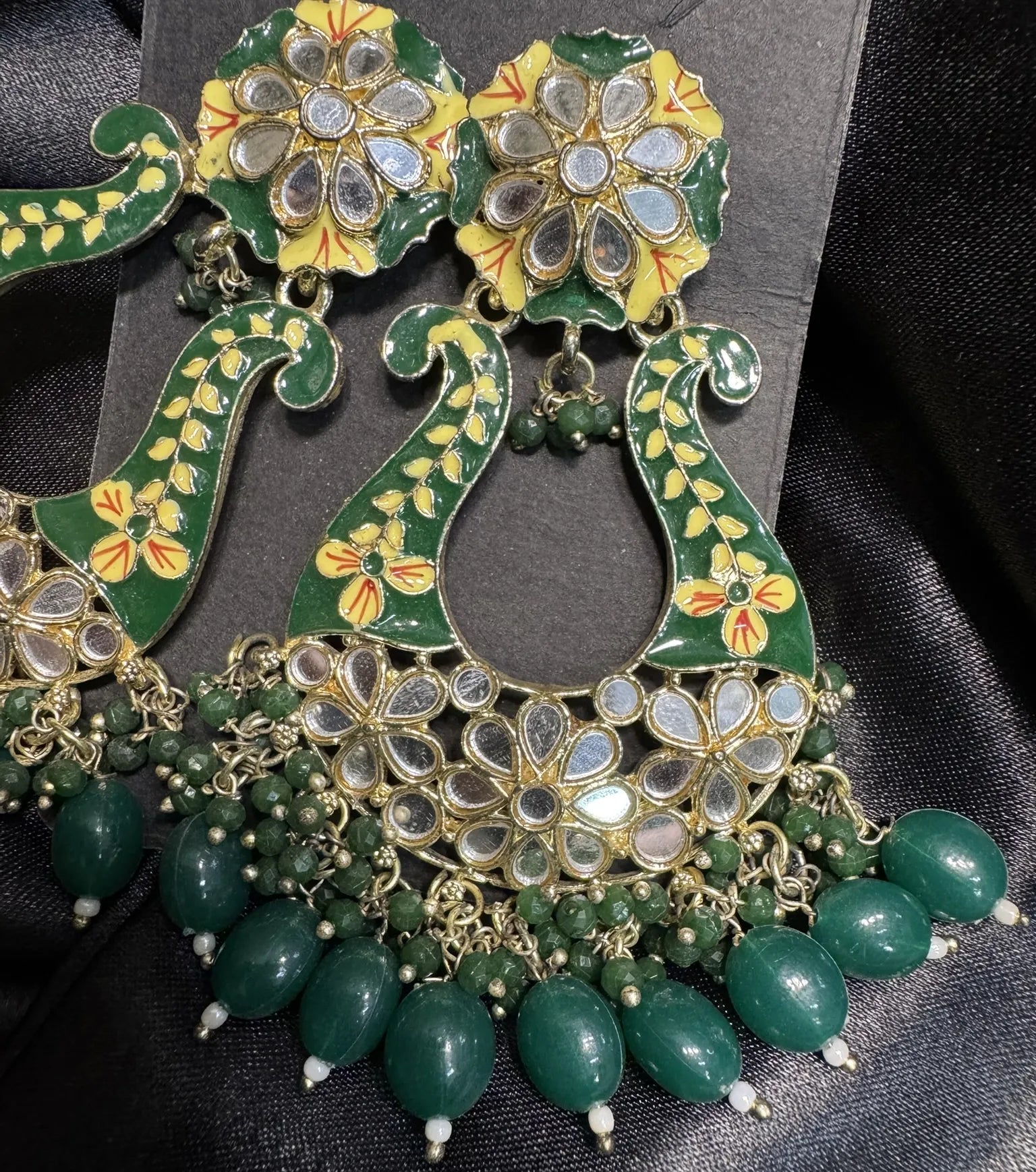 Ornate green and gold earrings with floral designs on a black background