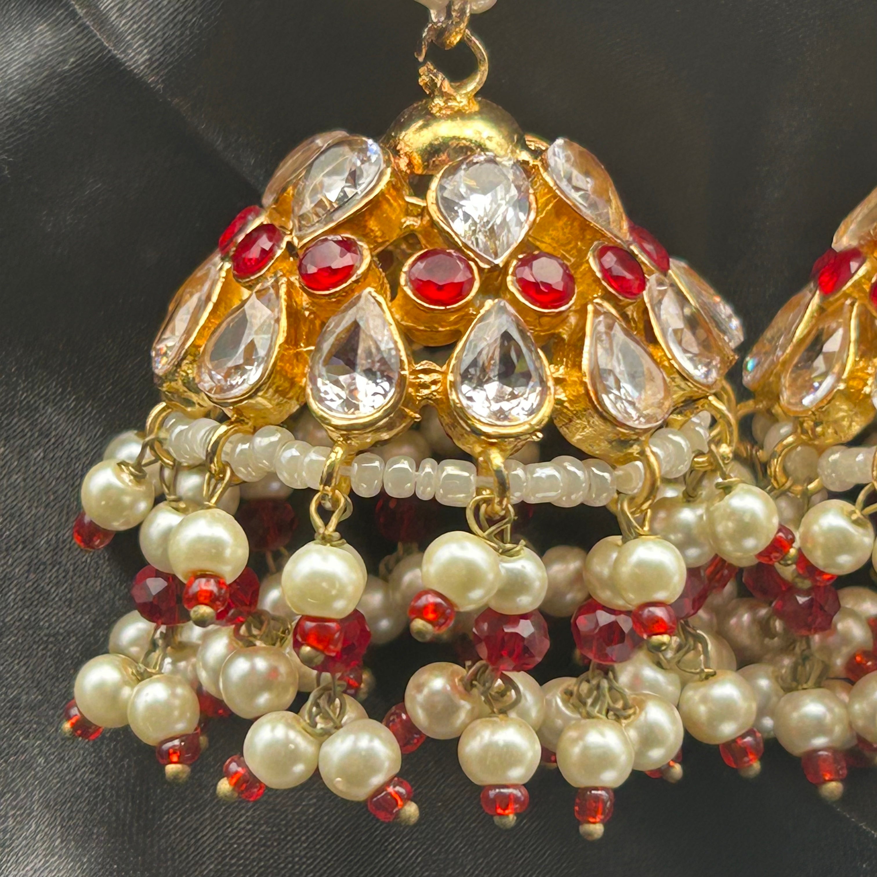 Ornate gold, red, and pearl earrings on a dark fabric background
