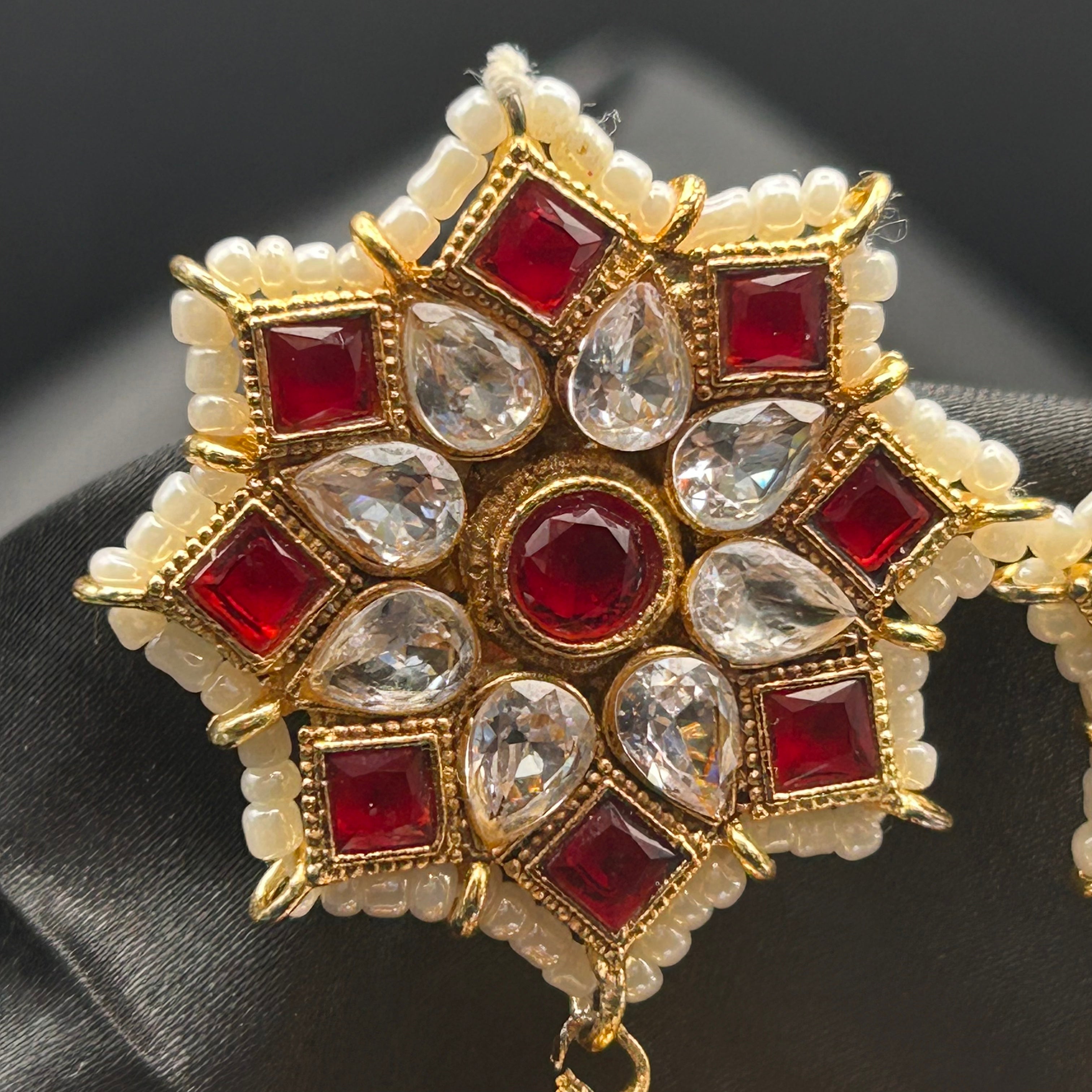 Ornate gold, red, and pearl earrings on a dark fabric background