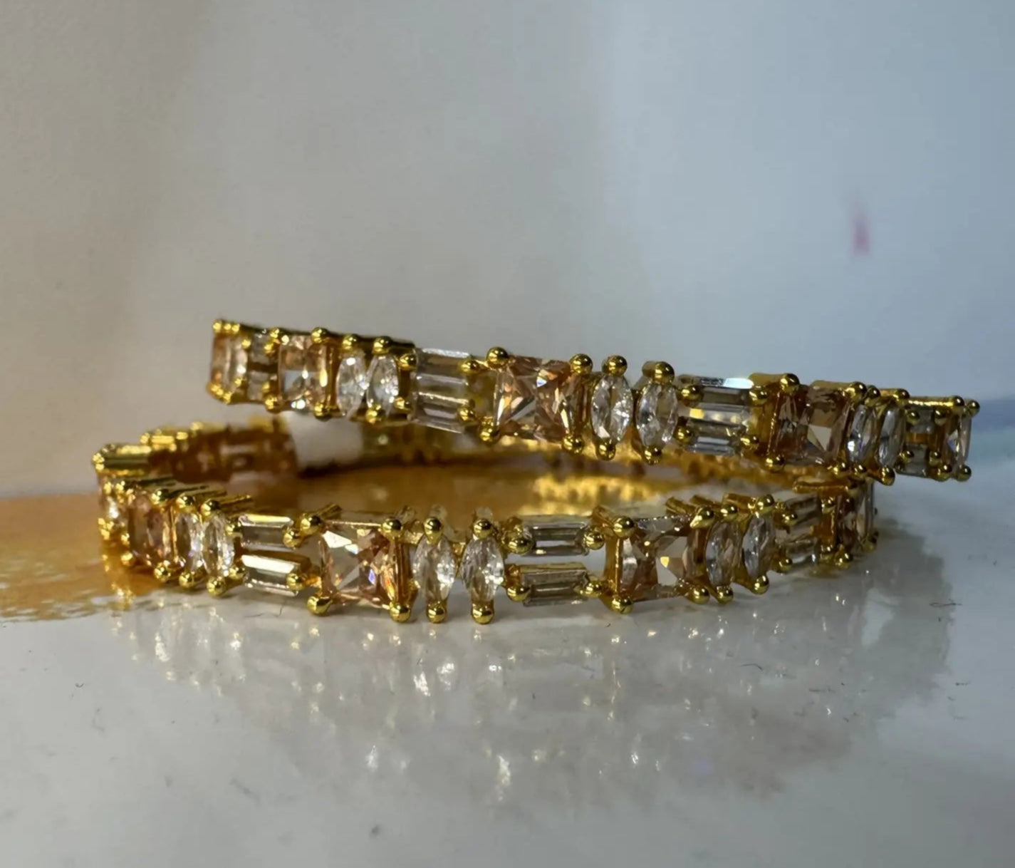 Gold plated bangles with clear gemstones in different patterns on a reflective surface