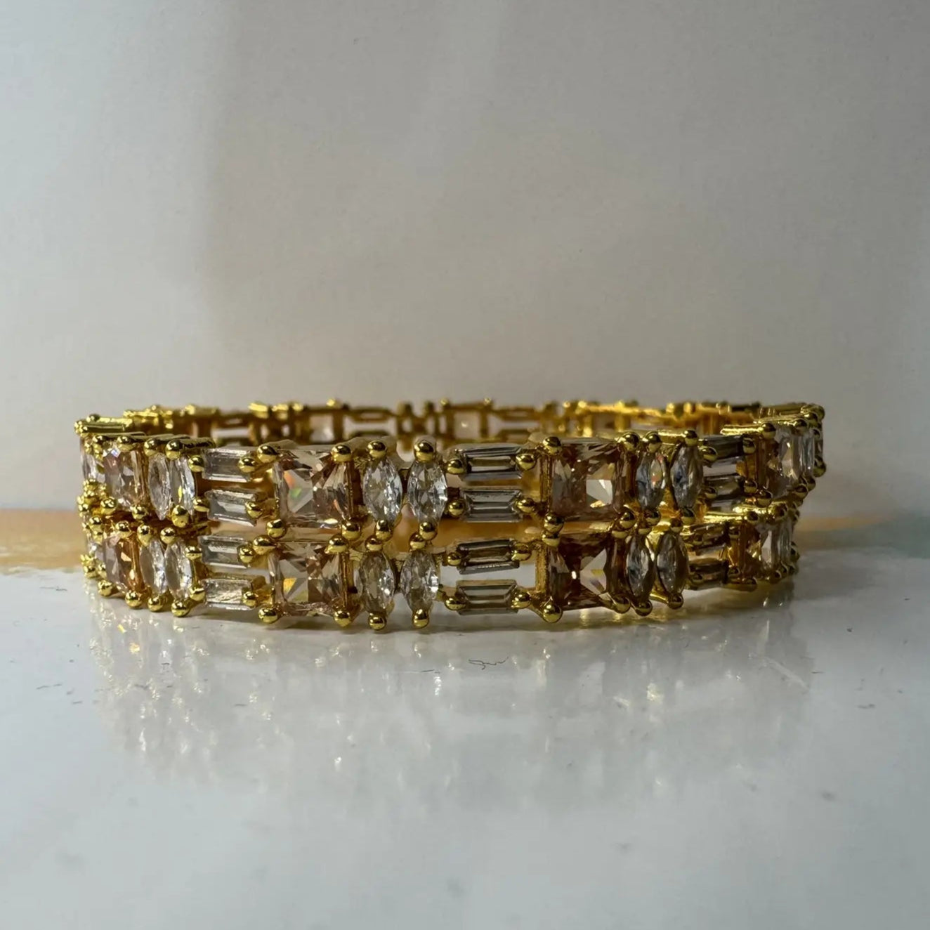Gold plated bangles with clear gemstones in different patterns on a white surface