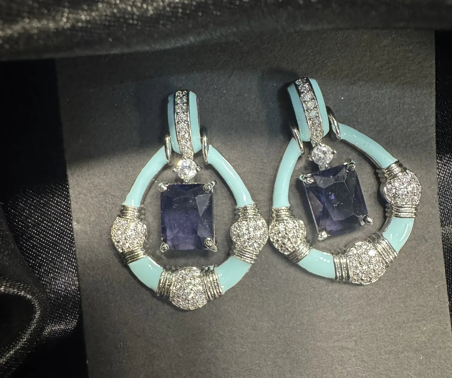 Pair of earrings with blue gemstones and turquoise accents on a black card.
