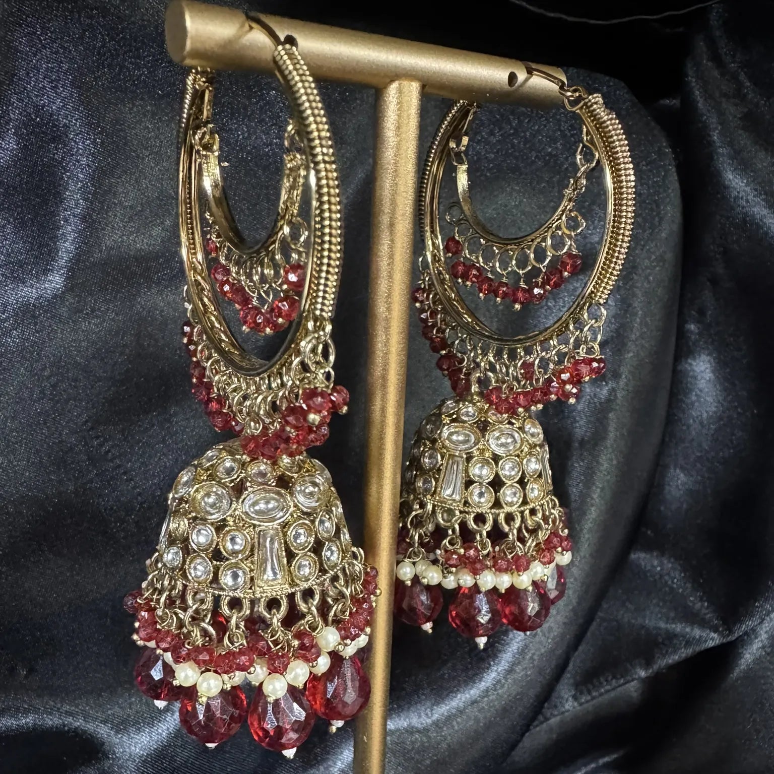 Pakistani design maroon and gold lightweight jhumkay on a stand against a dark background
