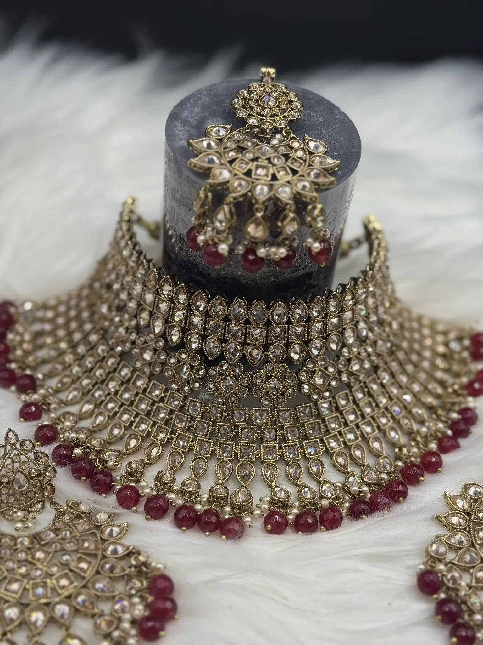 Ornate gold-plated, waterproof Indian bridal set with red hanging beads and matching teeka and earrings on a black background