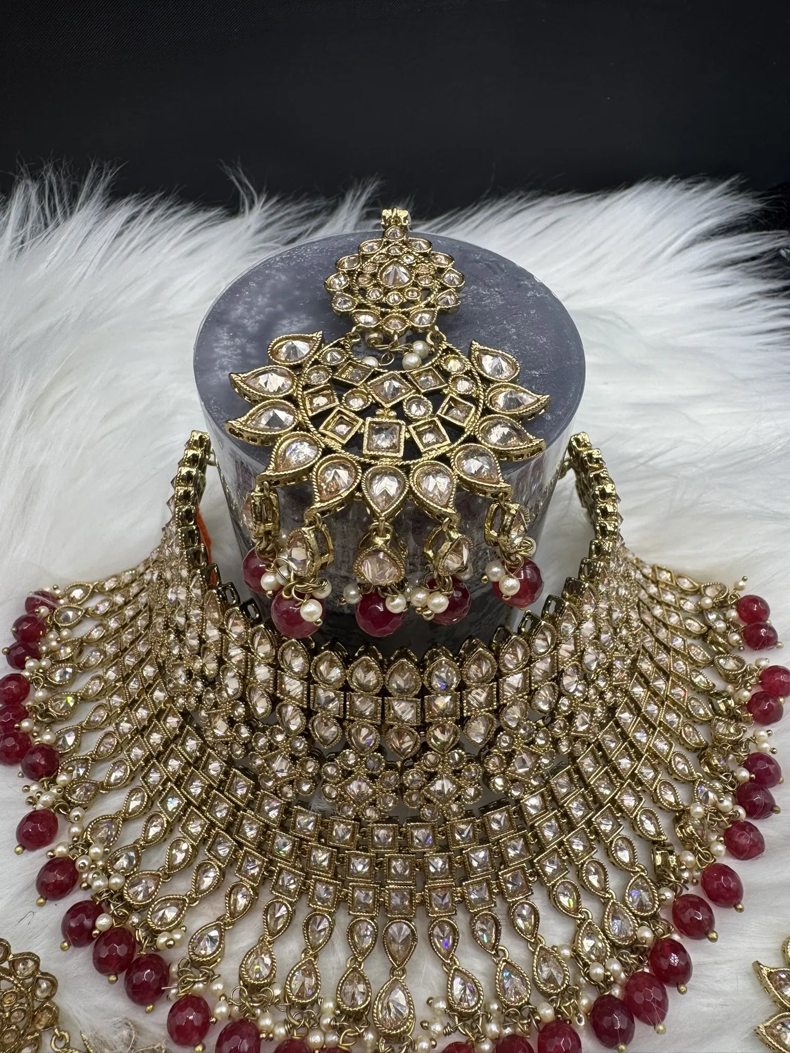 top view of gold-plated, waterproof Indian bridal set with red hanging beads and matching teeka and earrings on a black background