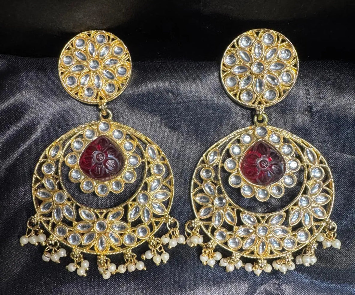 Ornate gold plated earrings with red gemstones on a dark fabric background