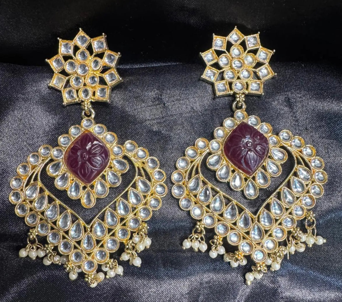 Ornate gold plated earrings with red gemstones on a dark fabric background