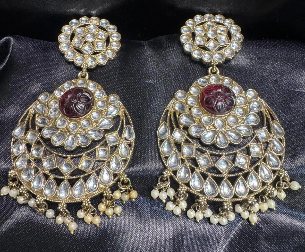 Ornate earrings with maroon gemstones on a dark fabric 