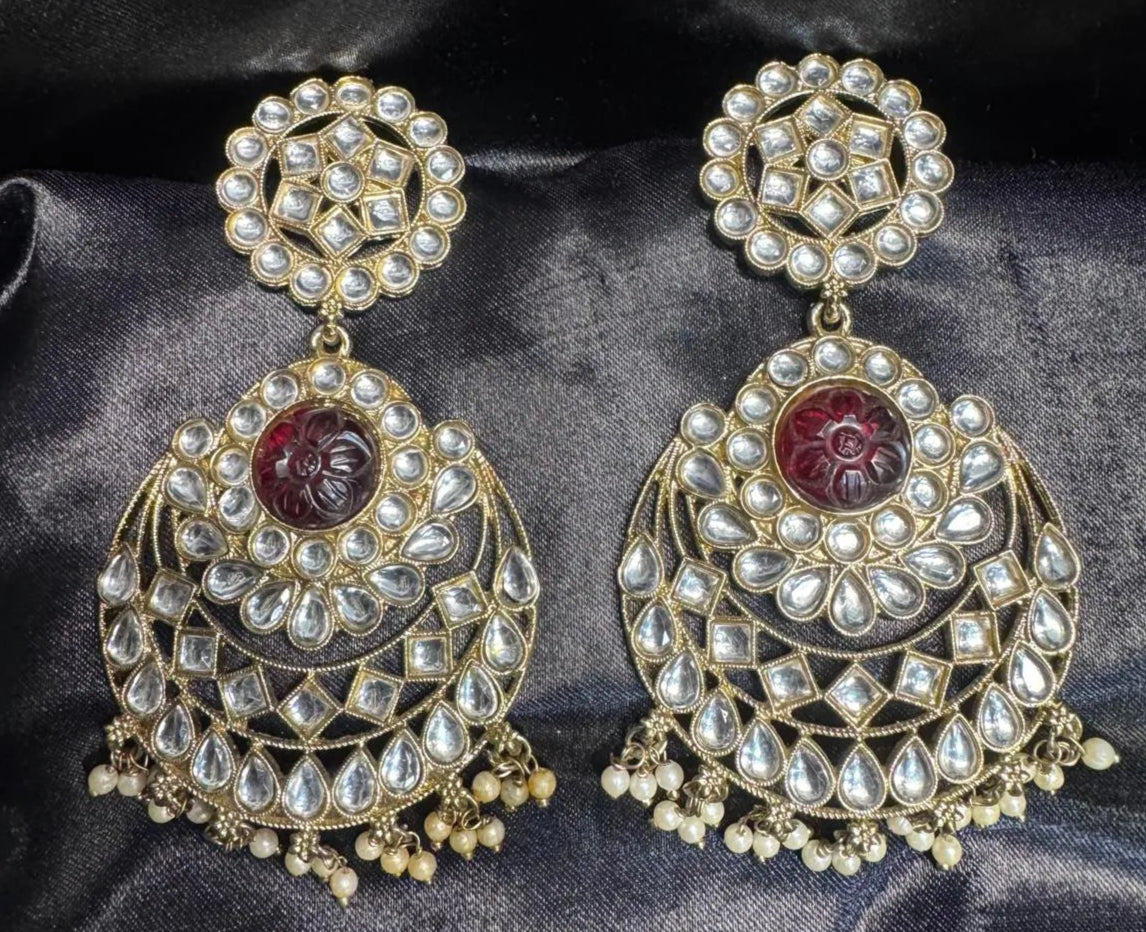 Ornate earrings with maroon gemstones on a dark fabric background