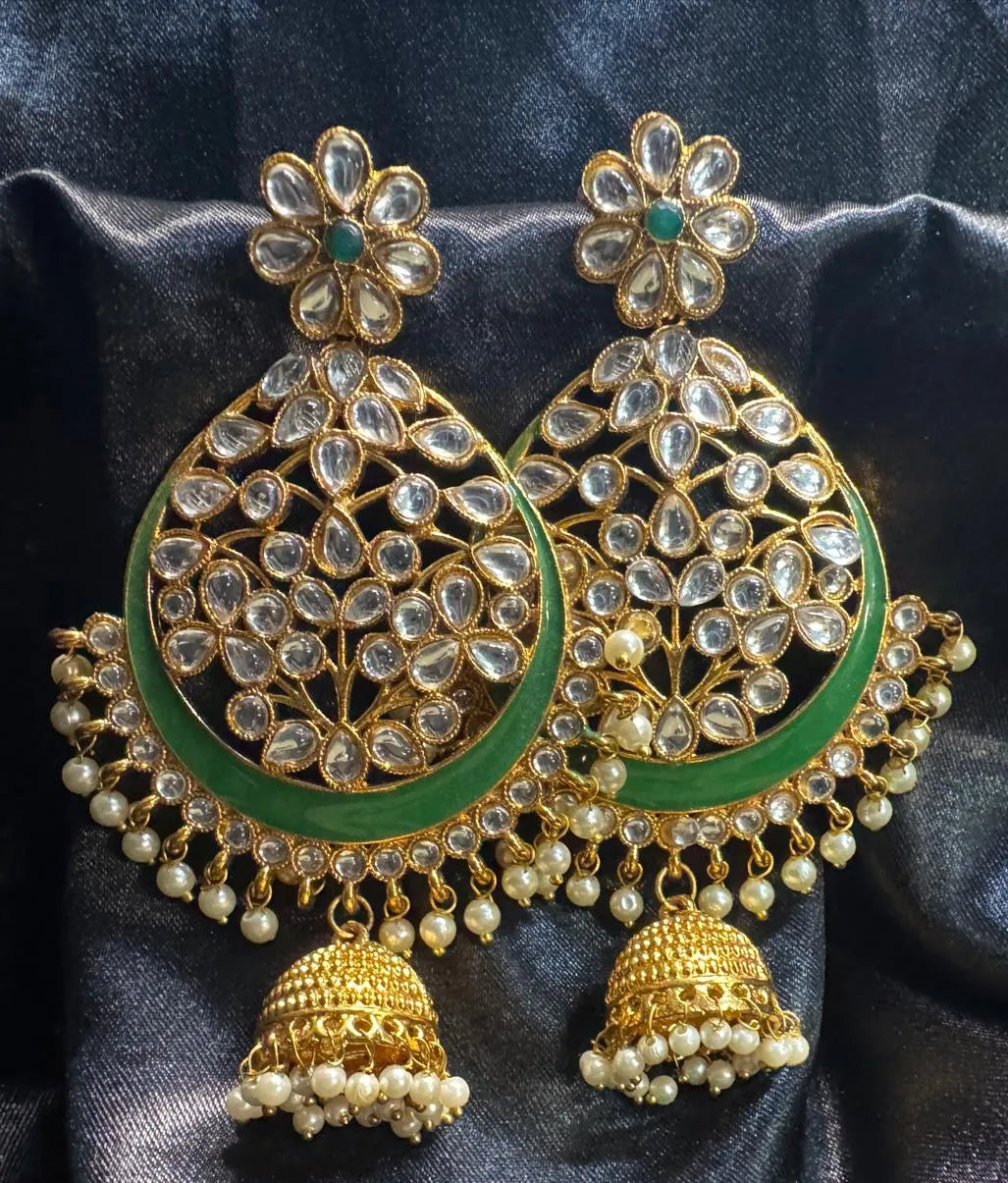Ornate gold and green earrings with pearl details on a dark fabric background