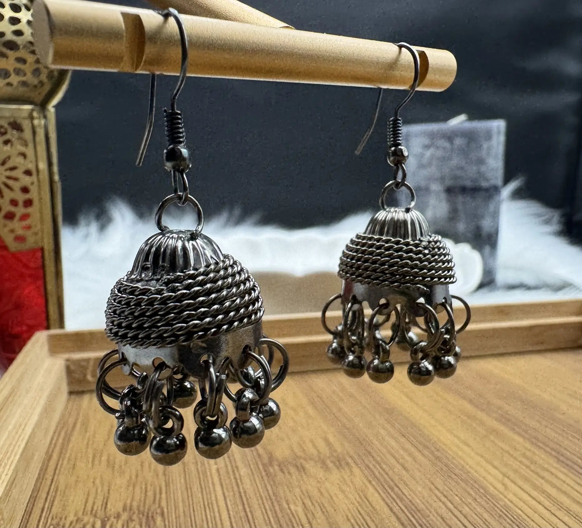 Pair of silver jhumka earrings on a wooden stand with a blurred background