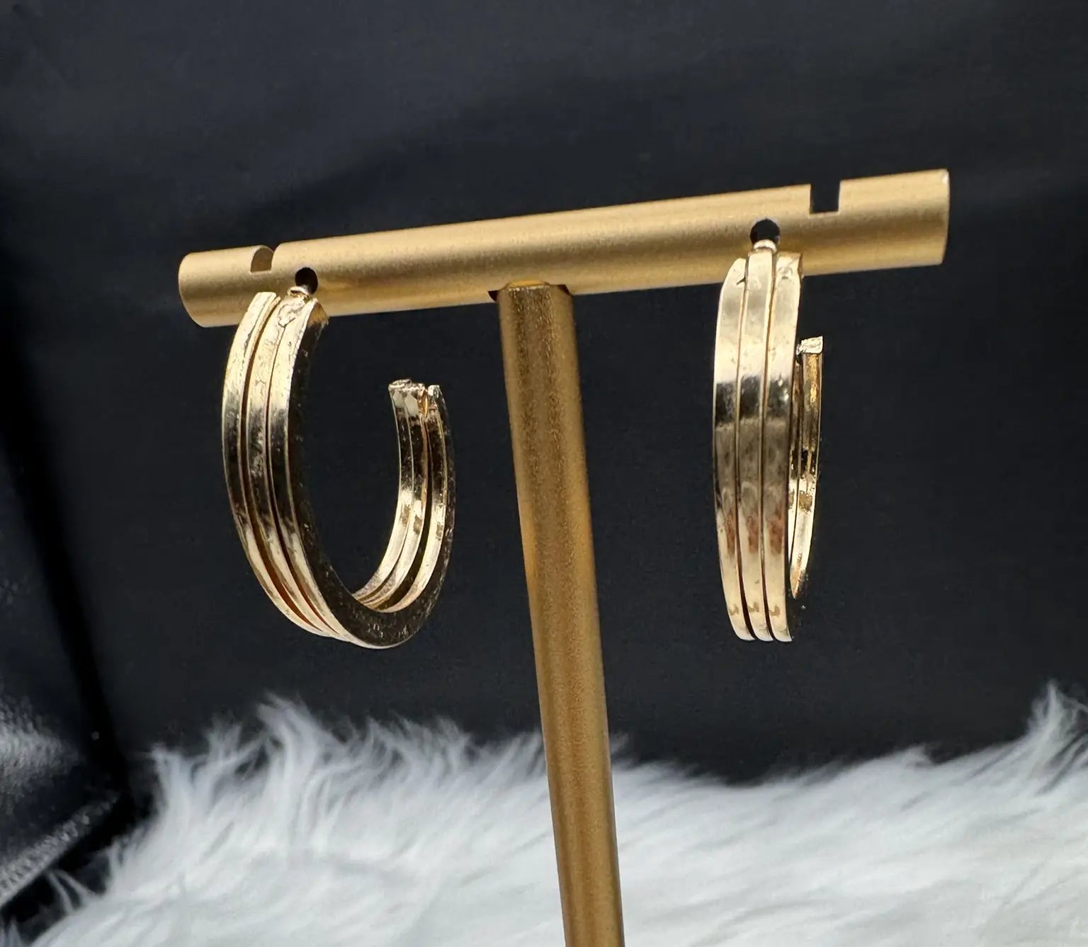 Gold plated hoop earrings on a gold stand against a black background