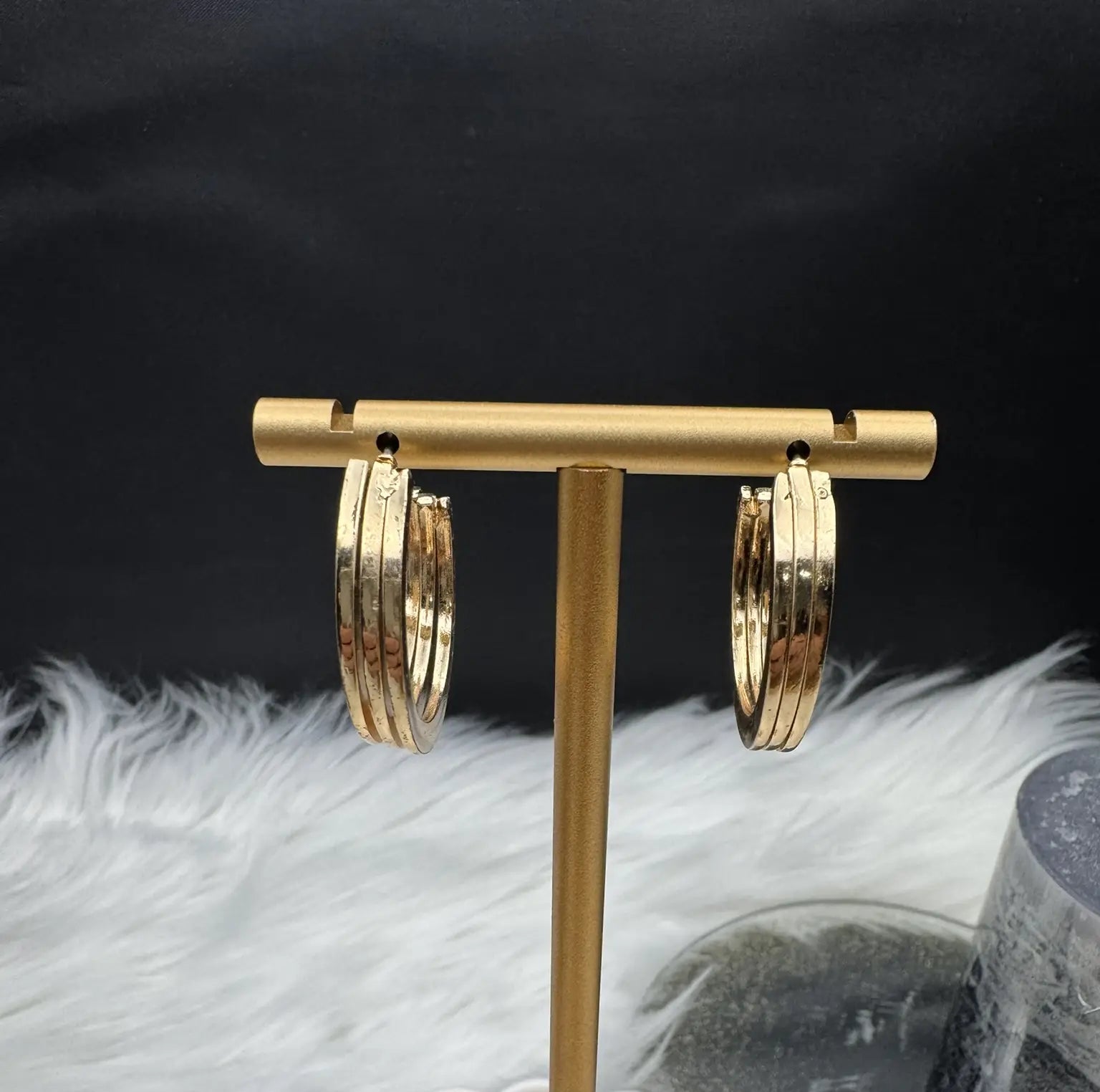 Gold plated hoop earrings on a gold stand against a black background with white feathers.
