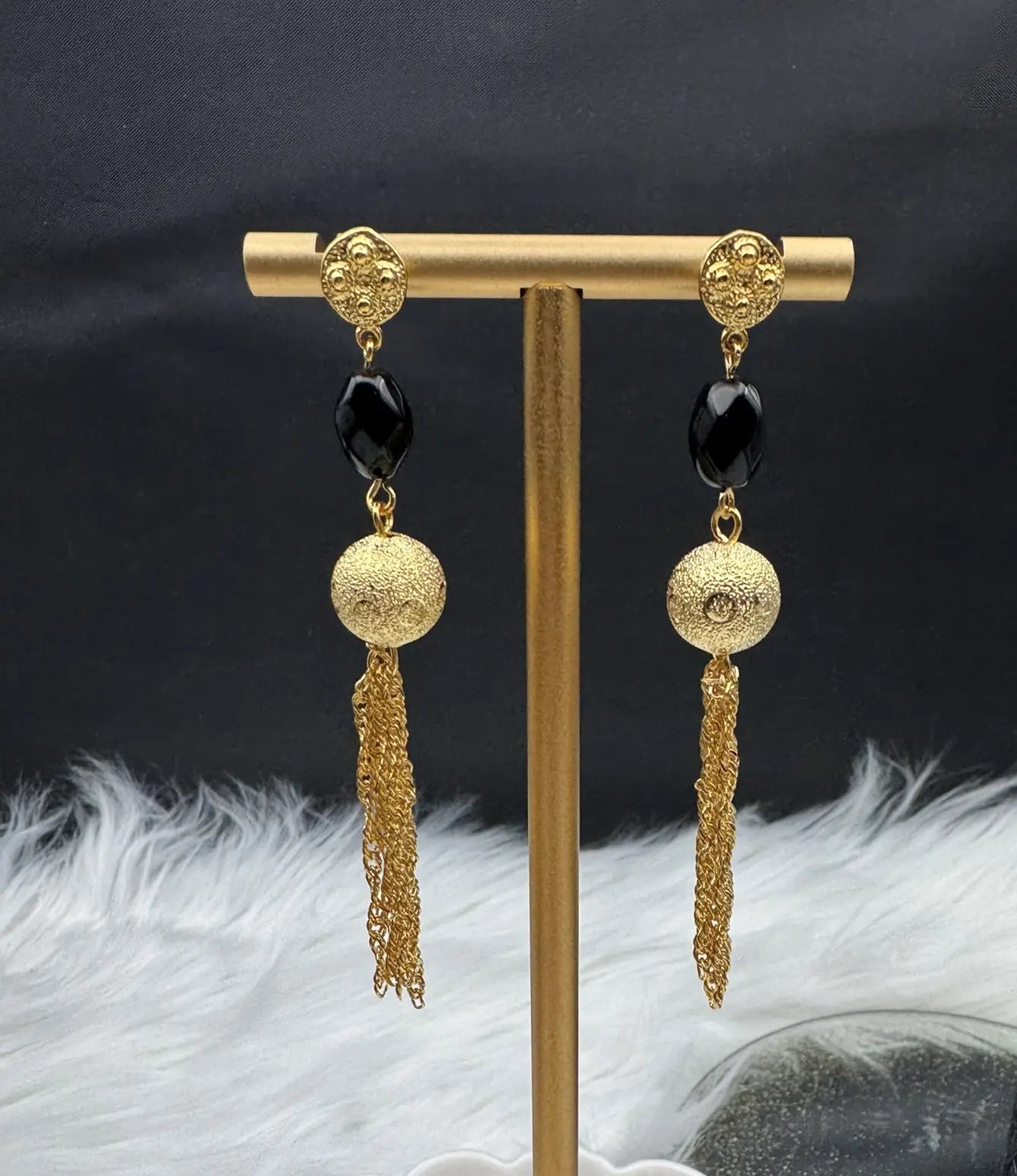 Gold and black earrings on a gold stand with a dark background