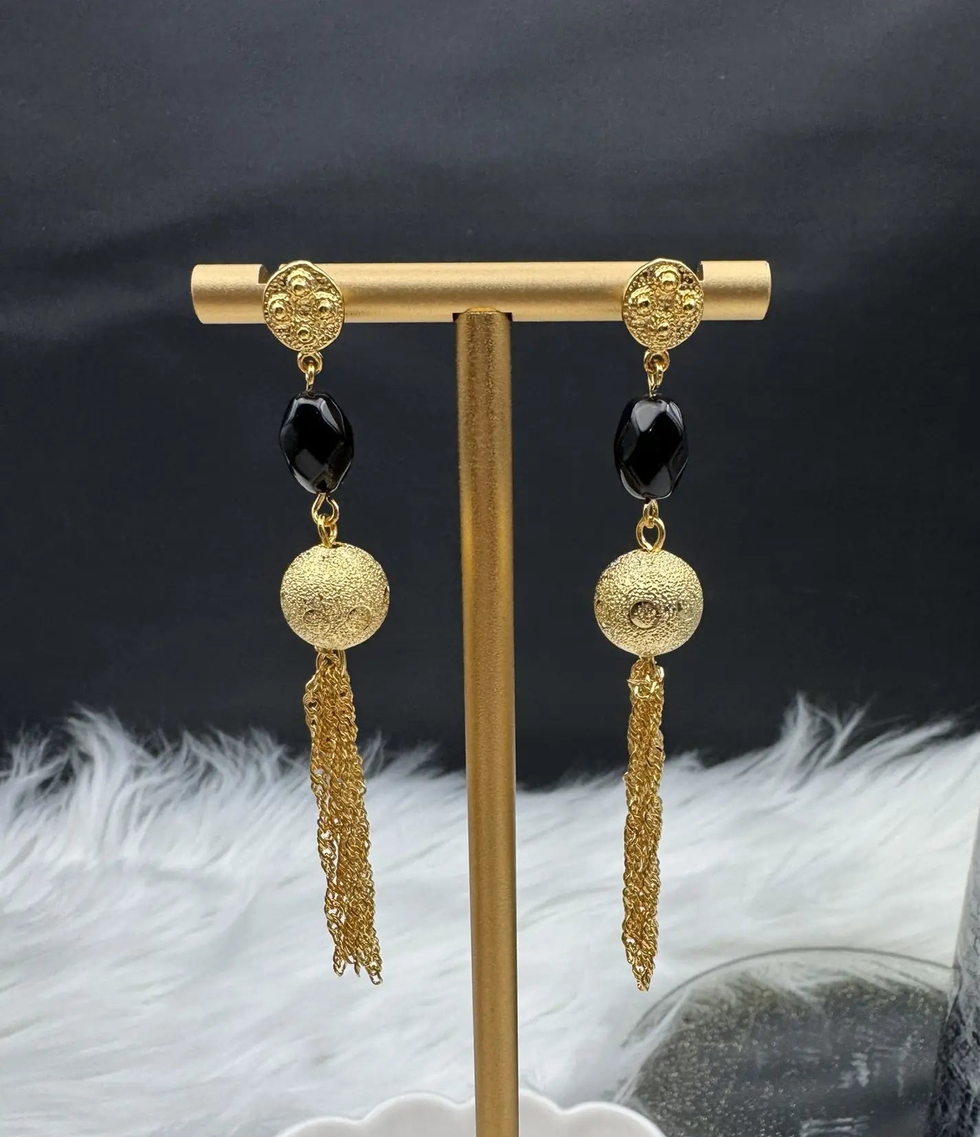 Gold earrings with black beads on a gold stand against a dark background