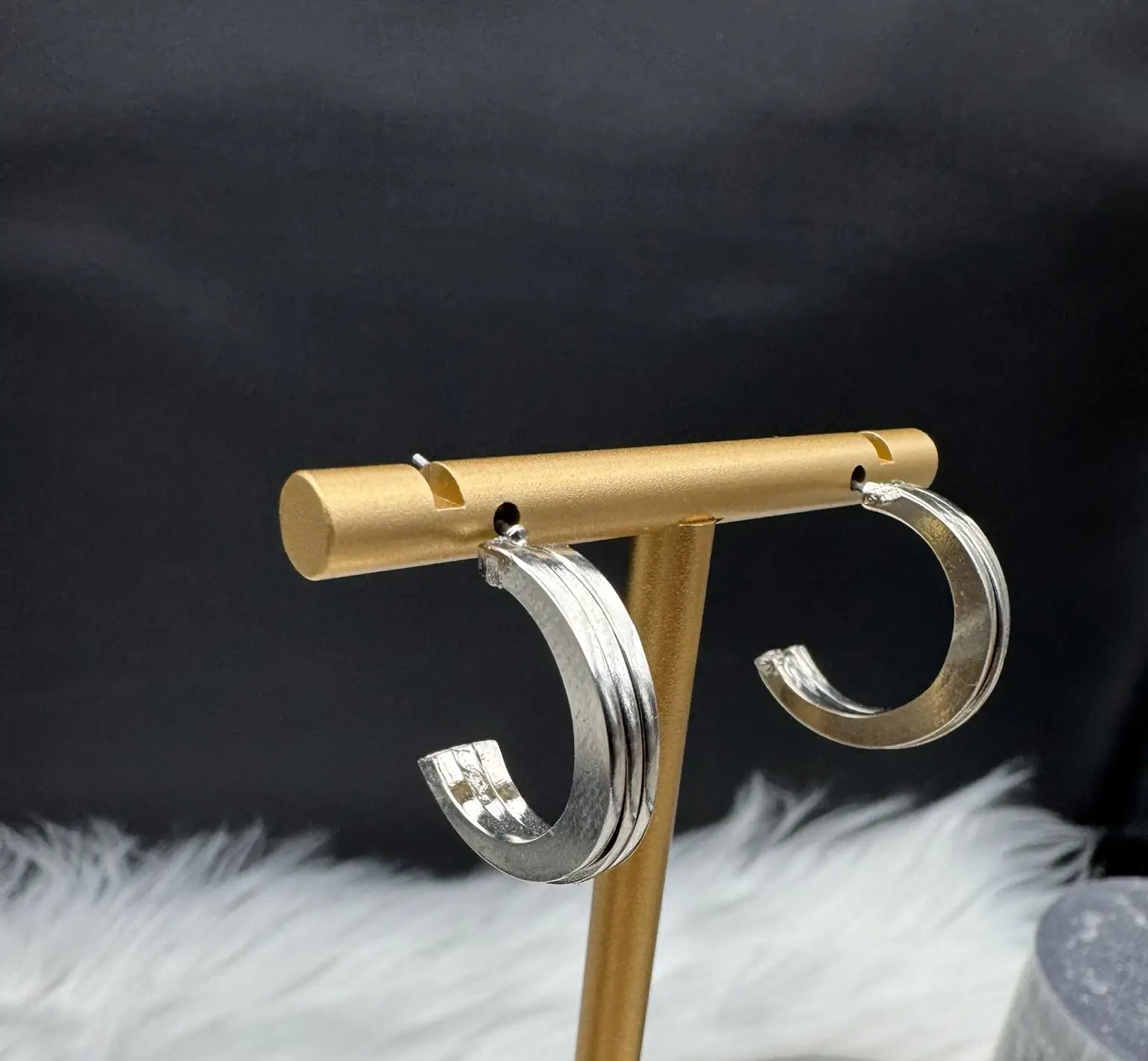 Silver hoop earrings on a gold T-shaped stand against a black background