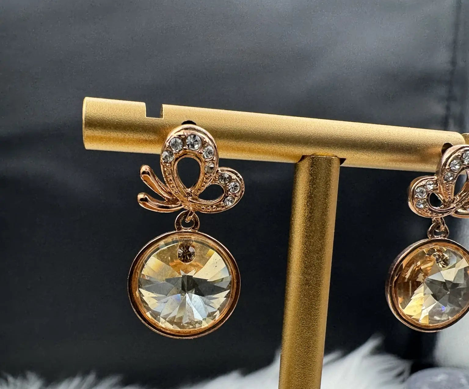 Gold earrings with clear gemstones on a gold stand against a black background