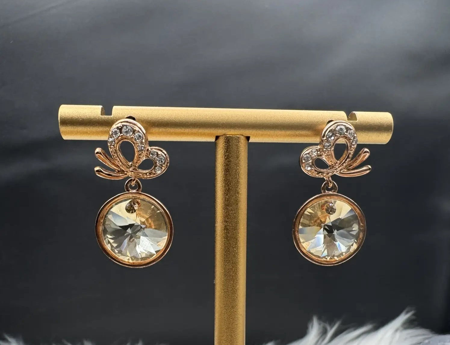 Gold plated earrings with crystal stones on a gold stand against a dark background